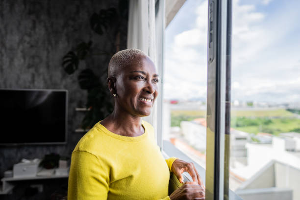 istock Mature woman contemplating while looking through the window at home 2201729231