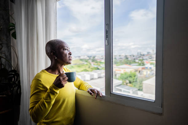 istock Mature woman contemplating while looking through the window at home 2201729237
