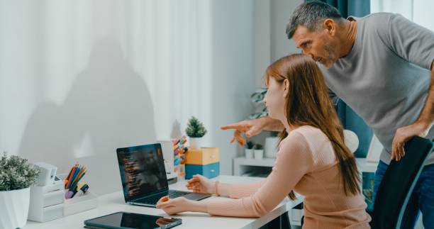 Senior father helps his daughter with her coding homework on laptop, family support and e-learning at home. Lifestyle family.
