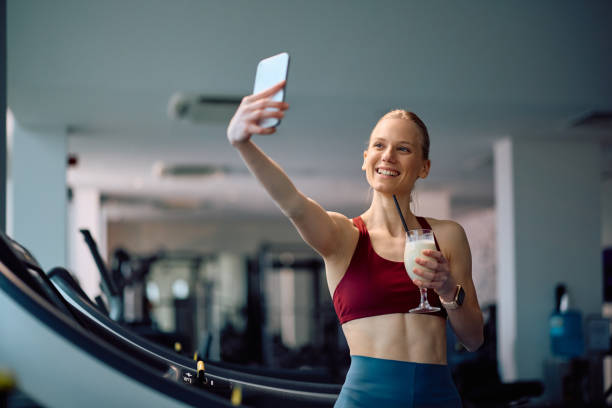istock Happy athletic woman drinking protein shake and taking selfie in a gym. 2201729480