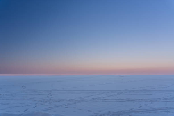 The tranquil beauty of a snowy Scandinavian landscape at sunset, located at Skutberget in Karlstad, Sweden. This aerial view highlights serene forests, snow-blanketed fields, and the peaceful lake of Vänern, reflecting the colorful hues of the evening sky.