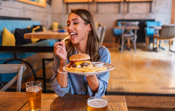istock Young woman eating burger at the restaurant 2201730755