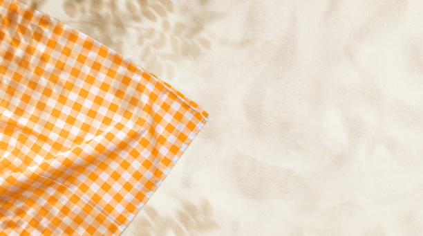A checkered orange and white picnic blanket partially laid on soft, textured sand, creating a summer and beach picnic atmosphere. The warm tones and empty space.not ai generated