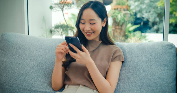 istock Young Asian woman smiling and looking at her smartphone while sitting in a bright, cozy cafe, enjoying a moment of relaxation. Cafe lifestyle. 2201734953