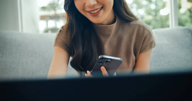 istock Young Asian woman speaking into her smartphone using voice command while working on a laptop in cafe. Cafe lifestyle. 2201734960