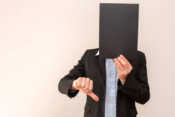 istock Businessman hiding face with black paper and showing thumbs down, expressing negative feedback 2201736099