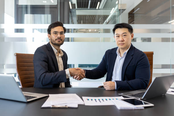 istock Two serious colleagues shaking hands. Serious and confident men in business suits sitting at a conference table and looking at the camera. 2201736990