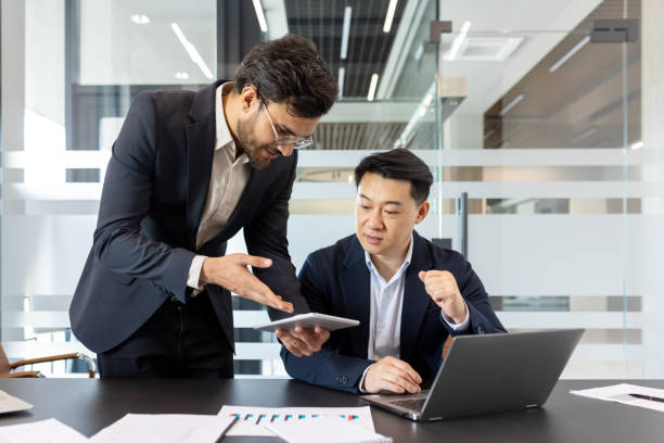 istock Two businessmen discussing a work project, a man in a business suit at his workplace inside the office. An employee demonstrates a work program on a tablet computer 2201737003