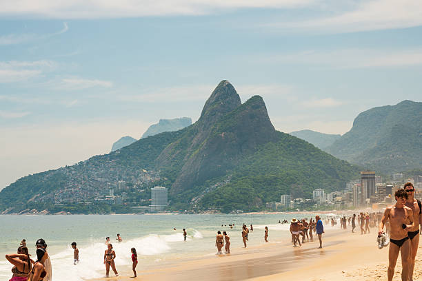 Ipanema, Rio de Janeiro, Brazil - January 18, 2025: Beachgoers at Ipanema Beach in Rio de Janeiro on a beautiful summer day with Morro Dois Irmãos in the background.