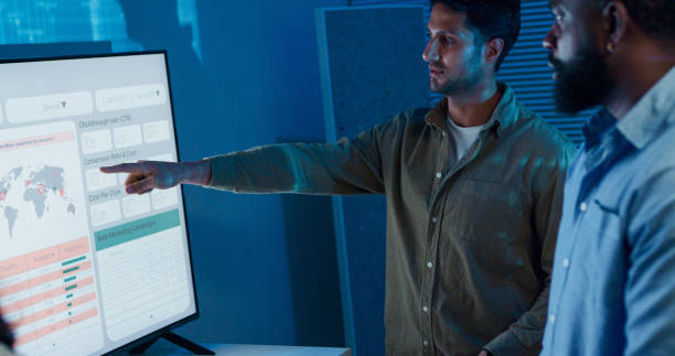istock Group of business professionals meeting working late discussing strategy and analyzing data on a large screen, collaborating on business growth standing at office night. Finance meeting. 2201740861
