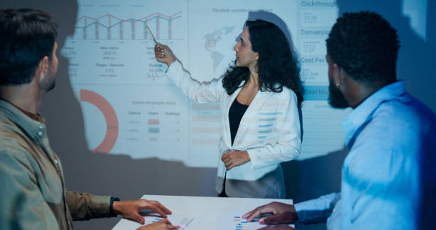 istock Group of businesspeople working late analyzing financial data displayed on projection screen while discussing strategy and planning for future business growth at office night. Finance meeting. 2201741669