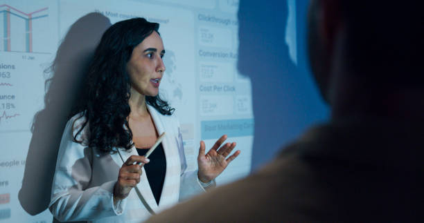 istock Group of businesspeople working late analyzing financial data displayed on projection screen while discussing strategy and planning for future business growth at office night. Finance meeting. 2201741672