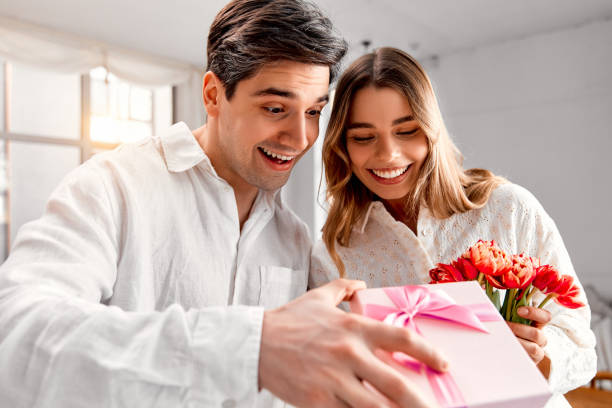 istock A happy couple in white outfits excitedly opening a pink gift box. 2201743190