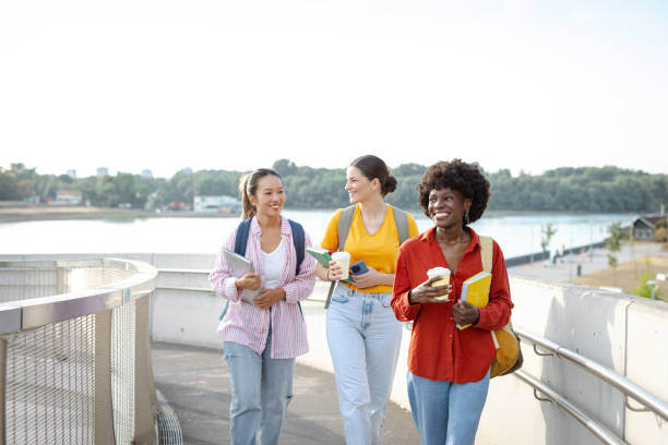 istock Three students walking together outdoors while carrying books and coffee cups 2201743890