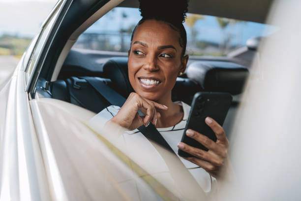 istock Smiling woman in a cab car with a cell phone in her hands 2201747546