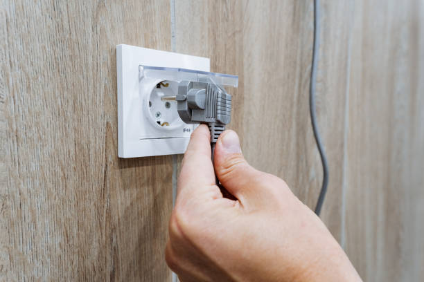 A person is carefully inserting a plug into an electrical outlet, which is a common and essential task required to supply power to various devices for their optimal usage and performance
