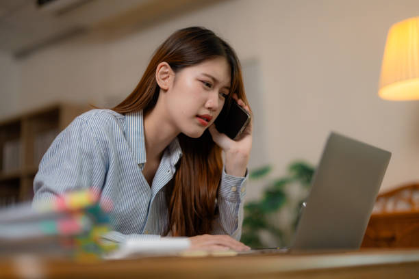 istock Professional Asian businesswoman experiencing stress, multitasking during late-night work with intense phone conversation and managing overwhelming job pressures 2201754351