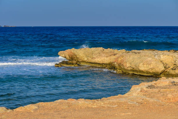 Gentle waves crash against ancient rocks, creating a tranquil moment on a sunny day by the shore.