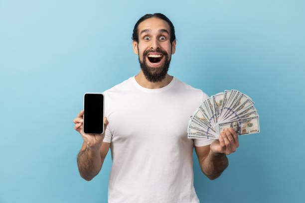 istock Man holding fan of dollar banknotes and smart phone with black empty display. 2201756661