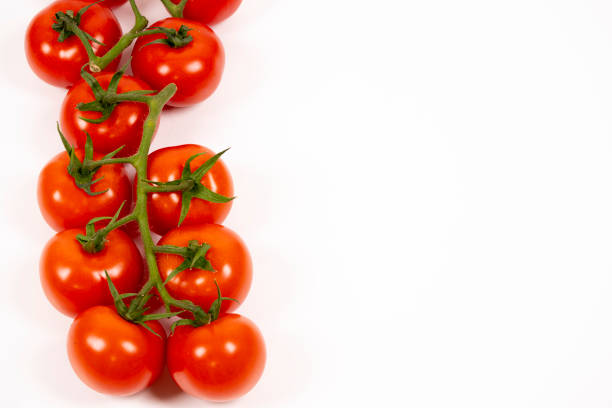 A cluster of ripe red tomatoes resting on a white surface showcases their shiny skin and lush green stems, emphasizing their freshness and quality.