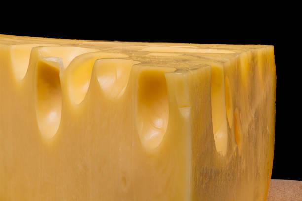 A wedge of cheese featuring prominent holes is showcased on a wooden surface against a dark background, highlighting its texture and color.