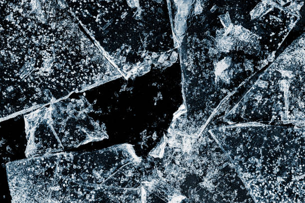 istock Hole, broken in a transparent textured ice. Crushed ice with cracks on a black background, close-up. 2201762664