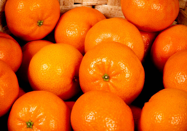 Vibrant tangerines fill a woven basket, showcasing their bright orange color. The setting suggests a local market overflowing with fresh produce.