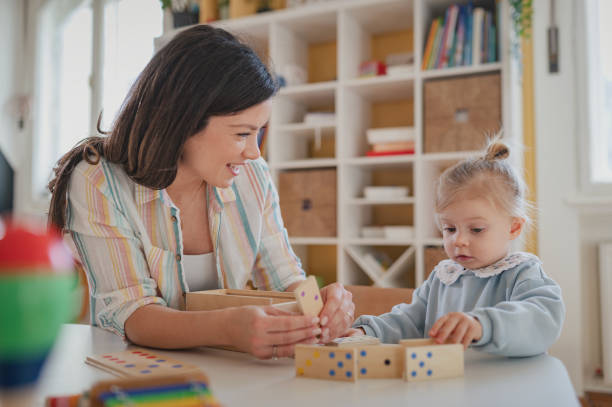 istock A caring young woman and a toddler engage in a hands-on learning activity with wooden Montessori toys in a bright, organized playroom 2201773813