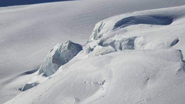 istock A rugged, snow-covered mountain landscape with ice formations and crevasses. The bright sunlight casts shadows, highlighting the jagged edges of the ice against the smooth snow. 2201775939