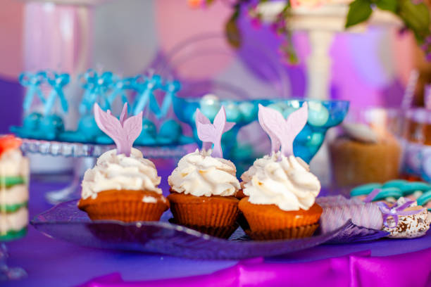 istock Birthday party concept for girl. Table for kids with cupcakes with withe topind decored purple mermaid tail. Summer season delicious on the party. Sea time theme on the candy bar 2201780326
