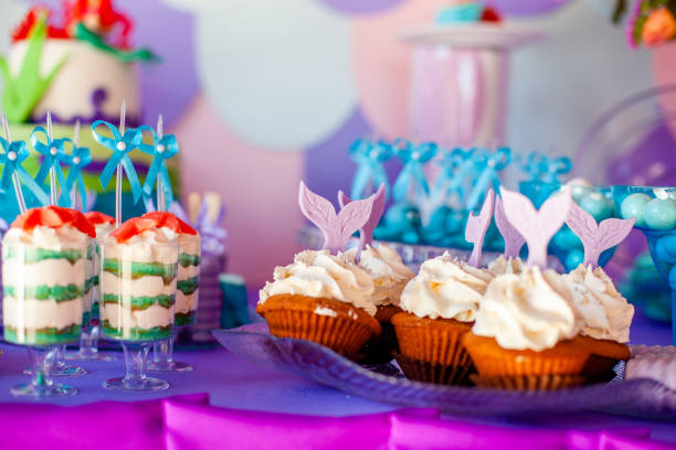 istock Birthday party concept for girl. Table for kids with cupcakes with withe topind decored purple mermaid tail. Summer season delicious on the party. Sea time theme on the candy bar 2201781027