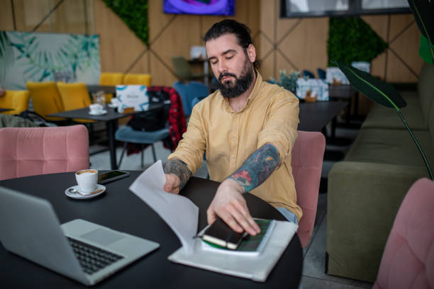 istock Young, bearded, tattooed man, in casual clothes, is working in cafe. 2201781858