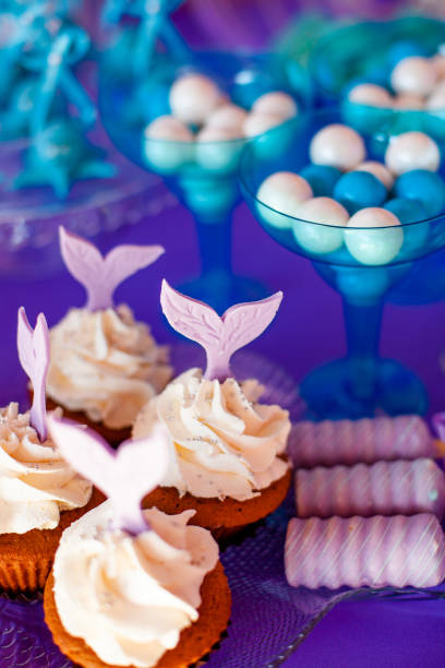 istock Birthday party concept for girl. Table for kids with cupcakes with withe topind decored purple mermaid tail. Summer season delicious on the party. Sea time theme on the candy bar 2201782120