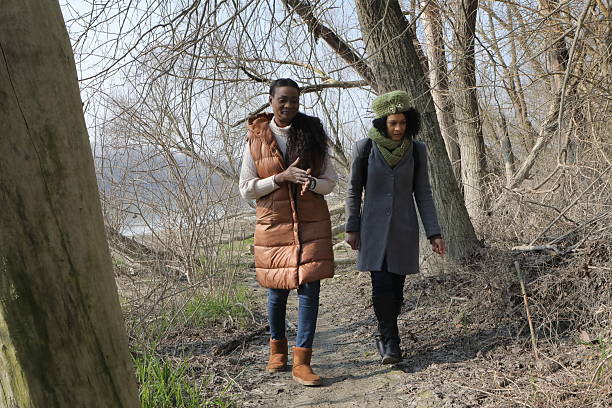 Four young women walk together along a nature trail, smiling and chatting