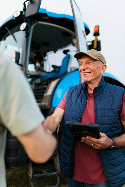 istock Smiling senior farmer holding a digital tablet meeting a man on farm 2201798434