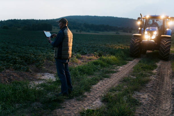 istock Senior farmer using digital tablet on agricultural field at dusk with tractor headlights 2201798560