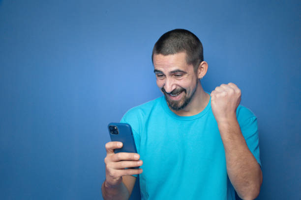 istock Happy young man celebrates with mobile phone on color background 2201798619