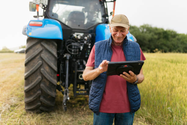 istock Happy elderly farmer on the farm field behind his tractor using a digital tablet 2201798642