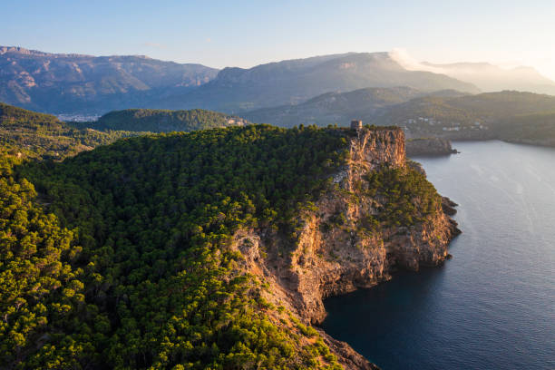 Aerial view coastline Port de Soller, Mallorca, featuring historic Torre Picada watchtower perched atop rocky cliffs. Deep blue Mediterranean Sea, breathtaking coastal scene