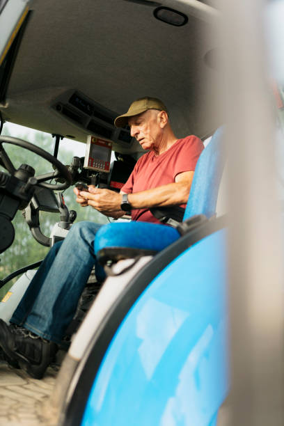 istock Elderly farmer sitting in tractor cabin with mobile phone 2201799130