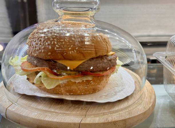 An incredibly mouthwatering cheeseburger elegantly displayed and protected under a beautiful glass dome. Close-up