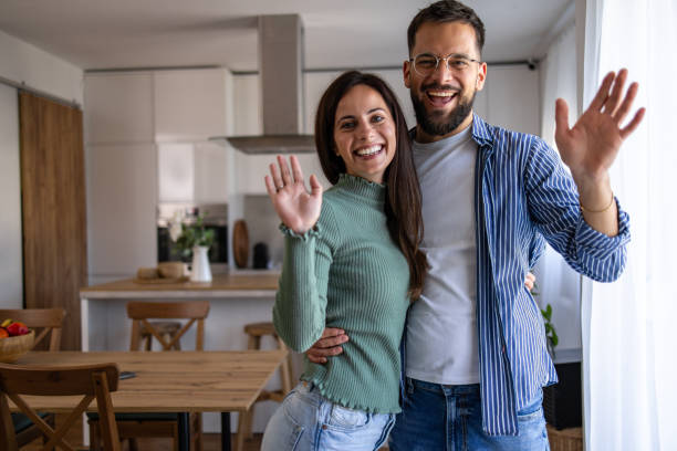istock Happy couple waving at the camera in their modern kitchen 2201801109