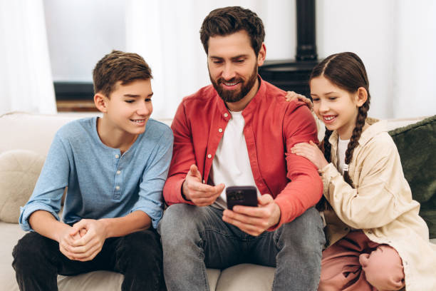 istock Father showing smartphone to his children while sitting on sofa at home 2201801659