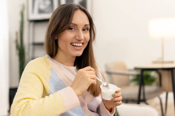 istock Happy woman enjoying yogurt on sofa at home 2201801673