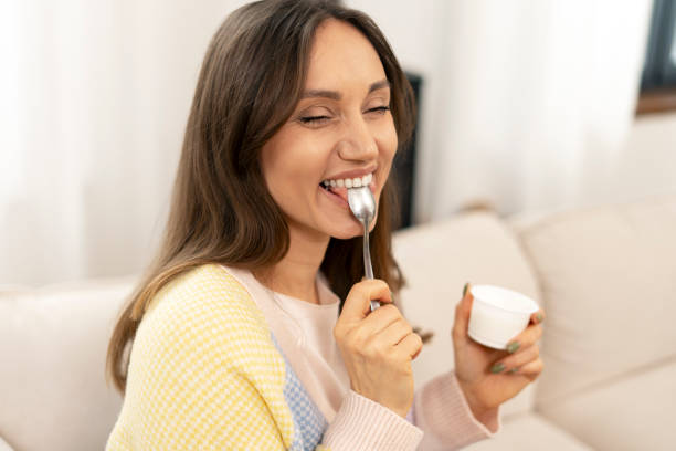 istock Happy woman enjoying yogurt on sofa at home 2201801678