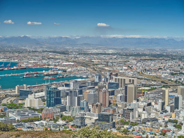 Explore the detailed landscape of Cape Town, showcasing its bustling harbor, urban buildings, and mountainous surroundings under a clear blue sky.