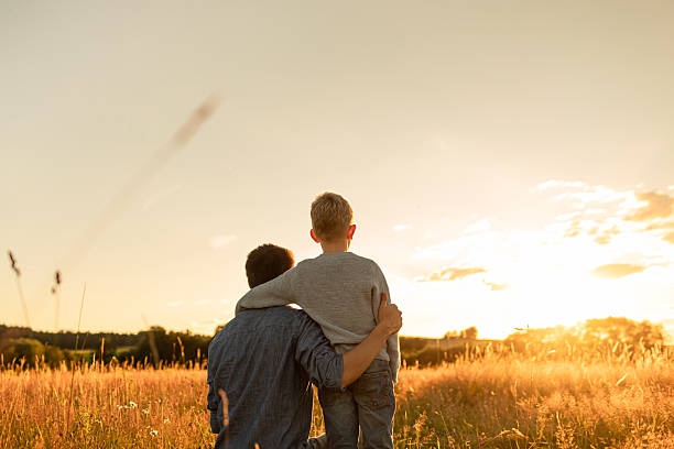 istock Happy father and son child watching the sunset together in a grass field 2201809072