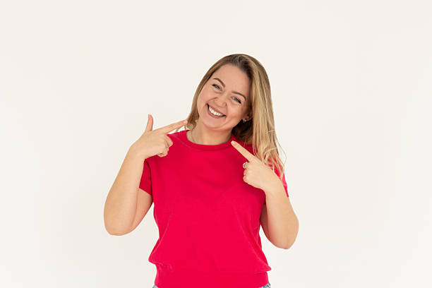 istock Young woman pointing fingers at her cheeks isolated over white background 2201814631