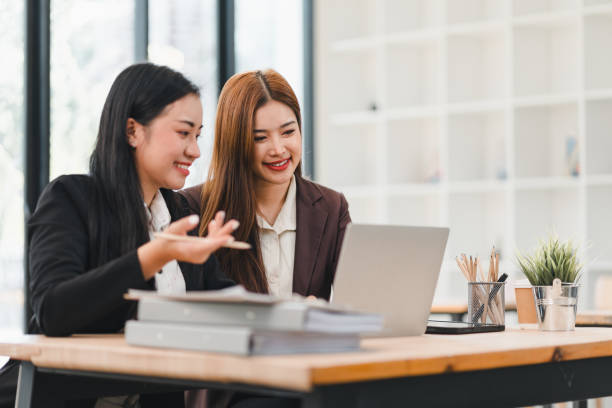 istock Two businesswomen discussing work while looking at laptop in modern office, with documents and stationery on desk, showcasing teamwork and collaboration 2201819315