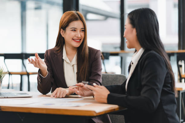istock Two businesswomen in formal attire having cheerful discussion at modern office table, with documents and laptop in front of them, showcasing teamwork and collaboration 2201819345